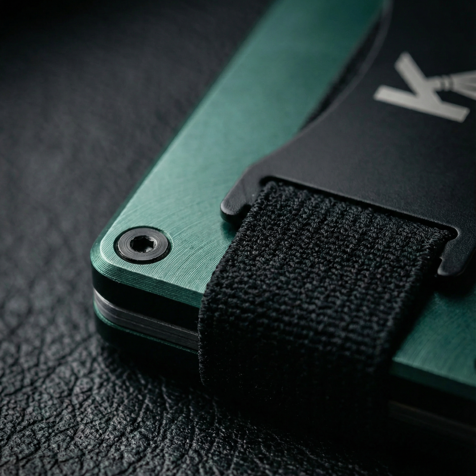 Green pocket knife with a black strap on a textured surface